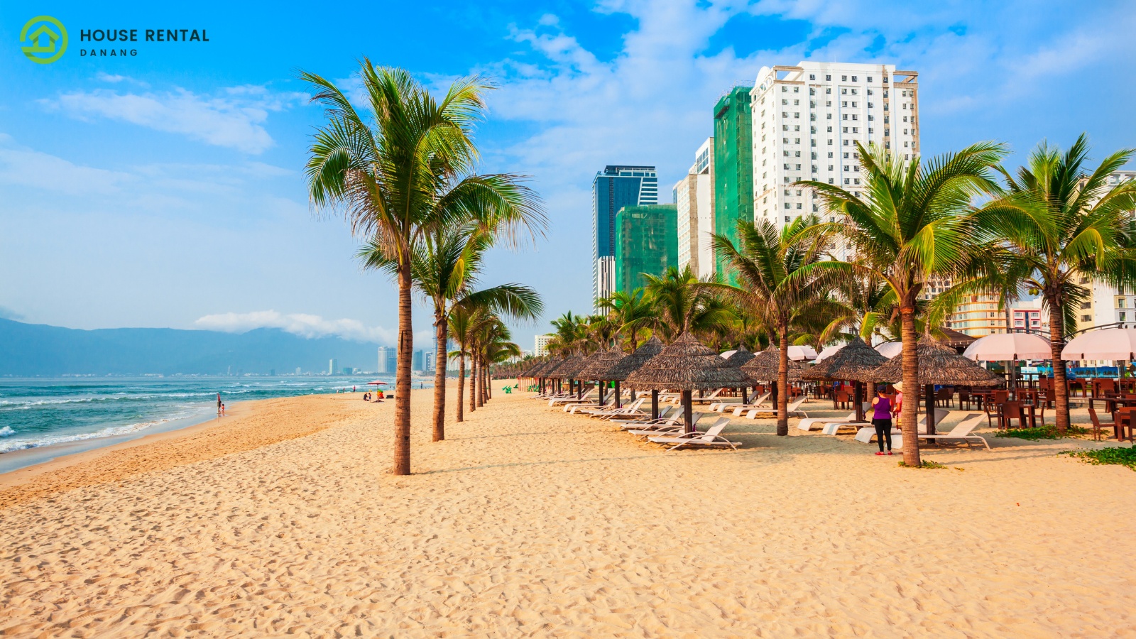 Best Places to Visit in Da nang - A beach with palm trees and buildings in the background.