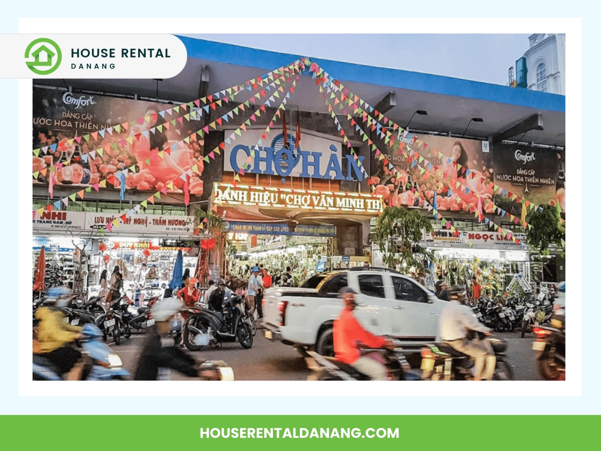 A bustling market scene at "Chợ Hàn," one of the best places for shopping in Da Nang, features numerous motorcycles, cars, and pedestrians passing by. The area is adorned with colorful flags and banners. Signs in Vietnamese are visible.