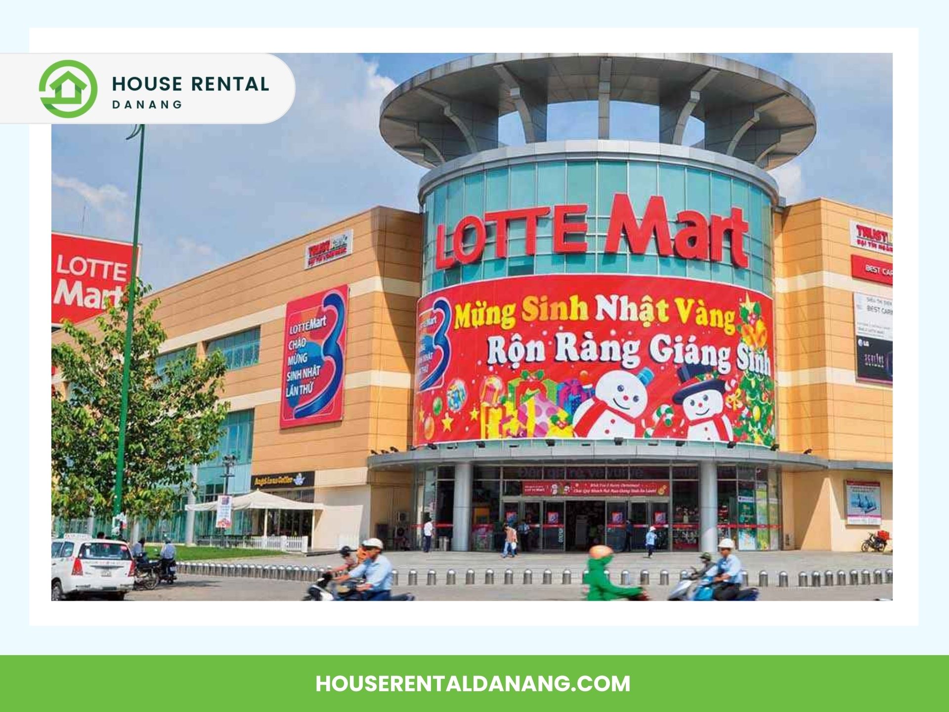 Exterior of Lotte Mart with a colorful holiday-themed banner, featuring festive decorations and Santa Claus. People on motorcycles are visible in the foreground, highlighting it as one of the Best Places for Shopping in Da Nang.