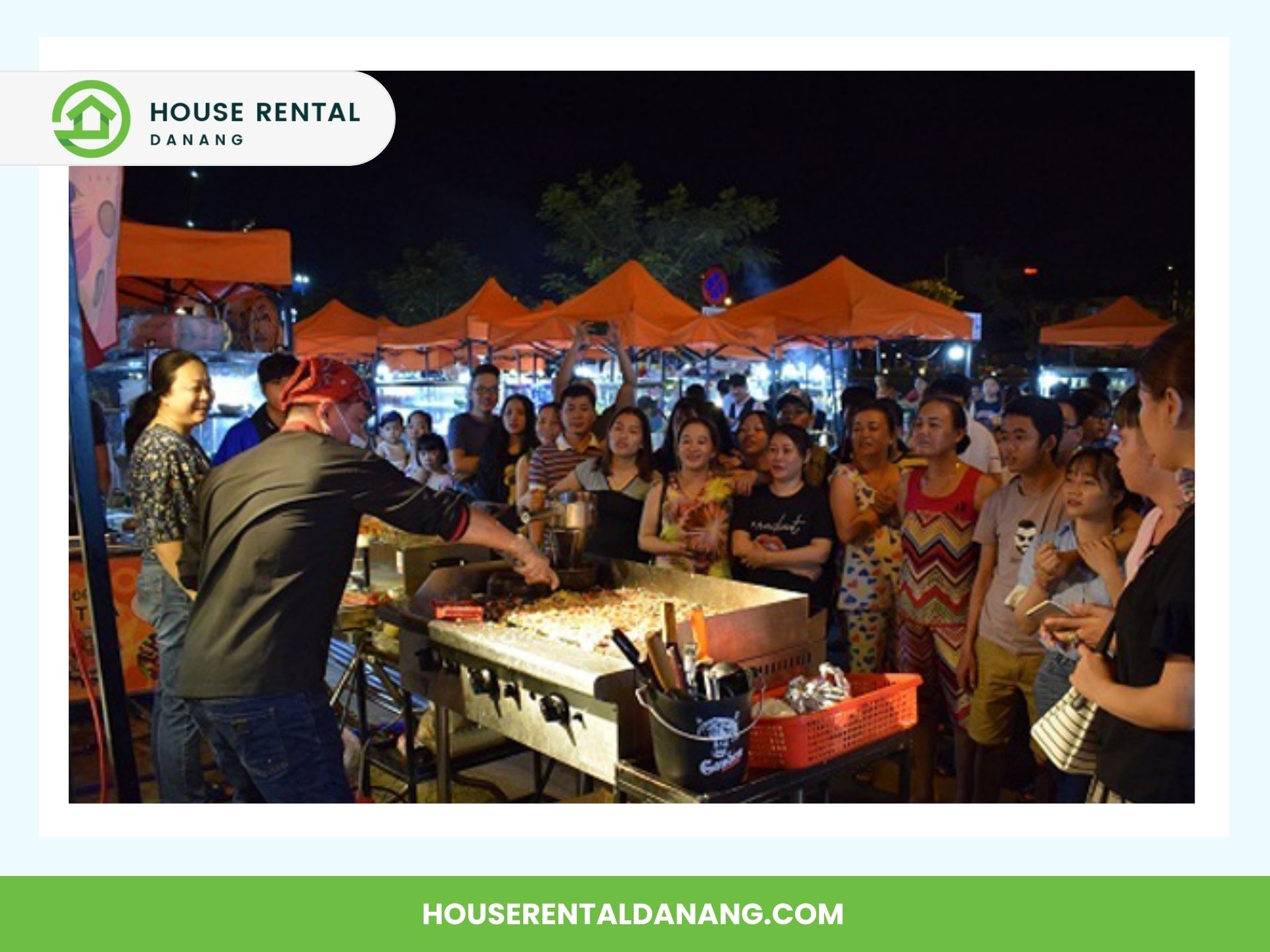 A chef cooking at an outdoor market stall as a crowd of people watches. Orange canopy tents are visible in the background, reminiscent of the vibrant Night Markets in Danang. House Rental Danang website details are displayed in the image frame.