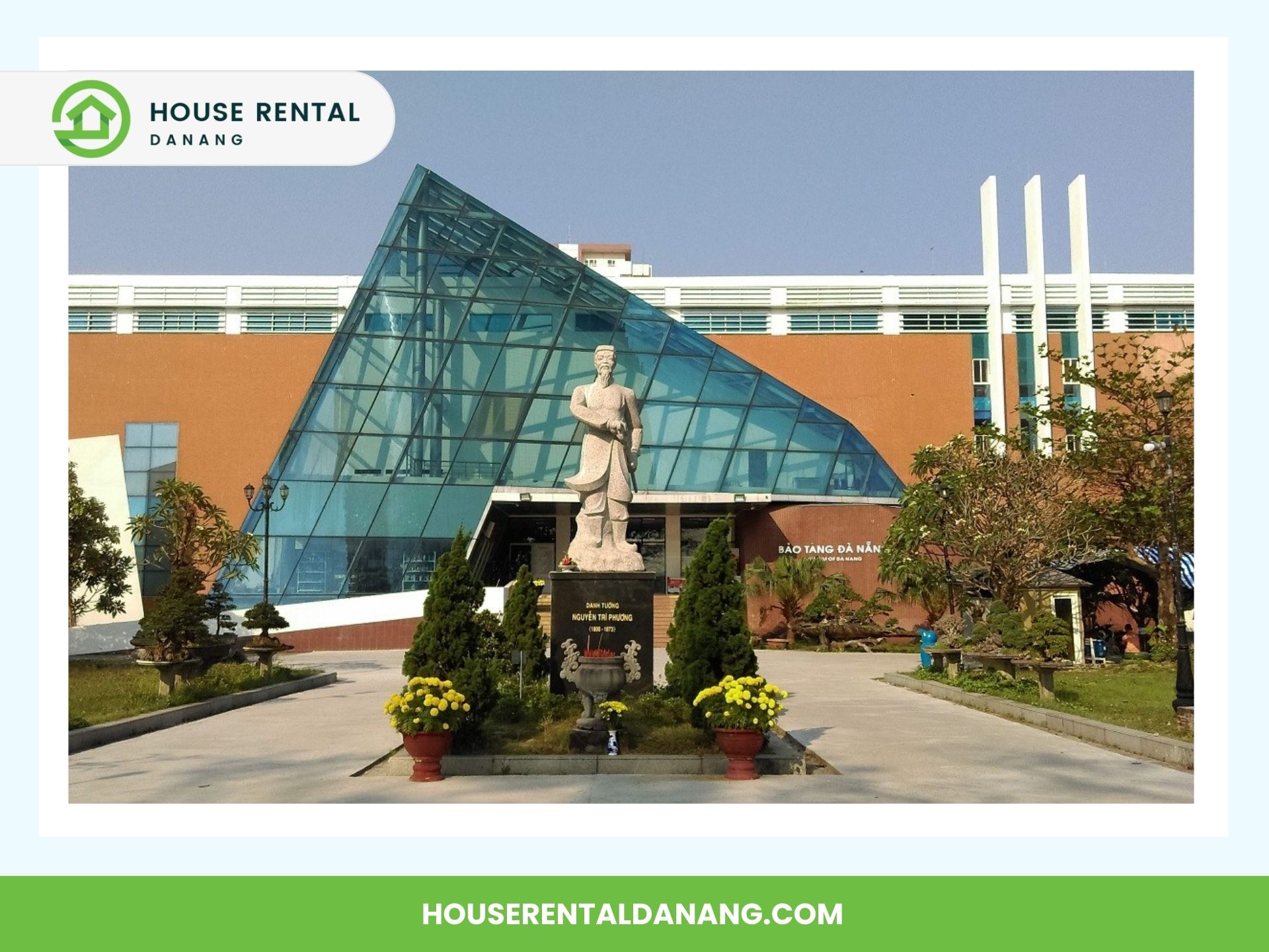 The image shows a modern building with a glass pyramid structure at the entrance, a statue in the forefront, and well-maintained greenery. The House Rental Danang logo and website URL are visible at the top and bottom. The style is reminiscent of architectural highlights found in Da Nang, Vietnam.