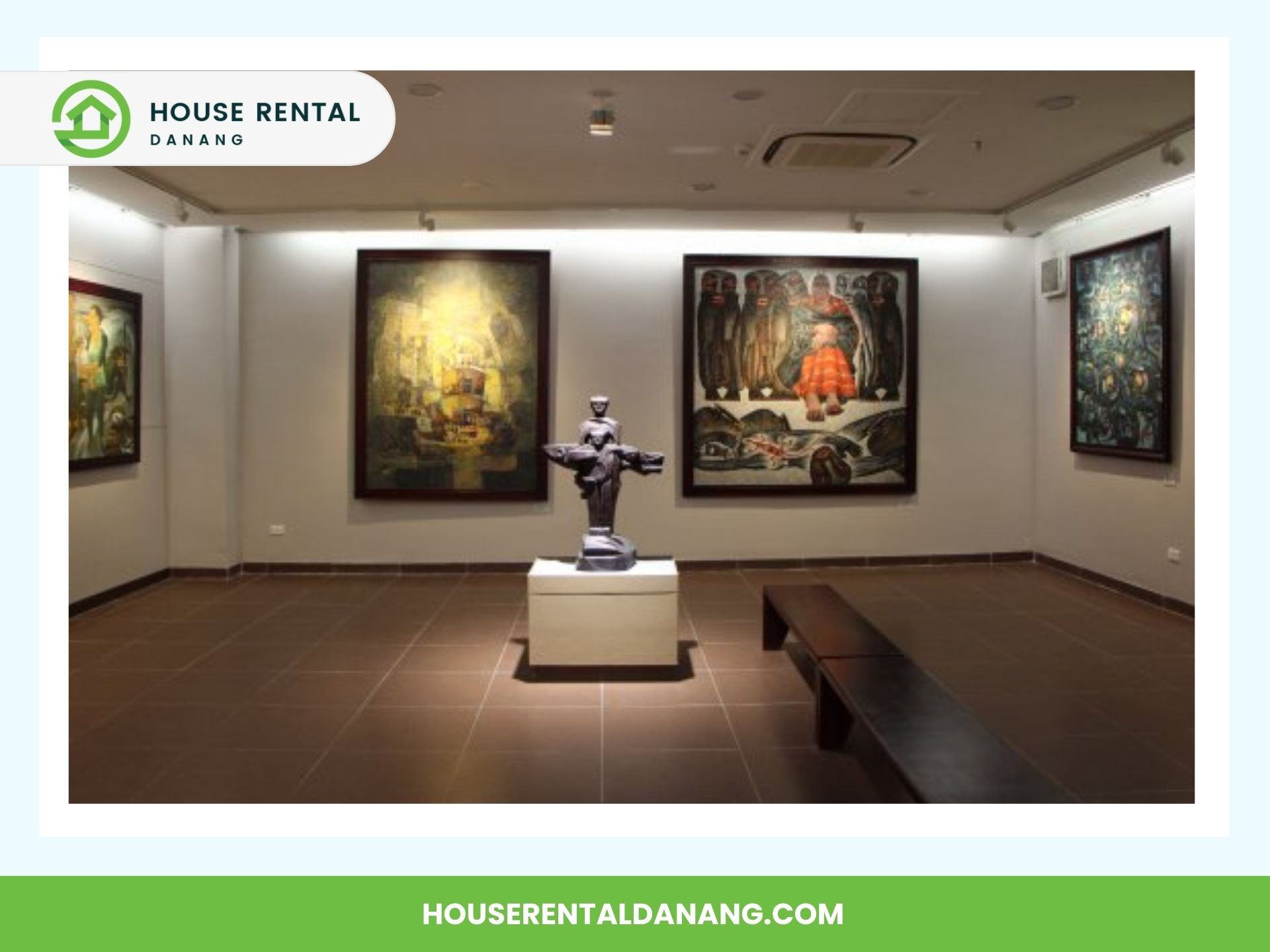 A small art gallery at the Da Nang Fine Arts Museum features several framed paintings on the walls and a central modern sculpture on a pedestal. The room has a brown tiled floor, a black bench, and overhead lighting.