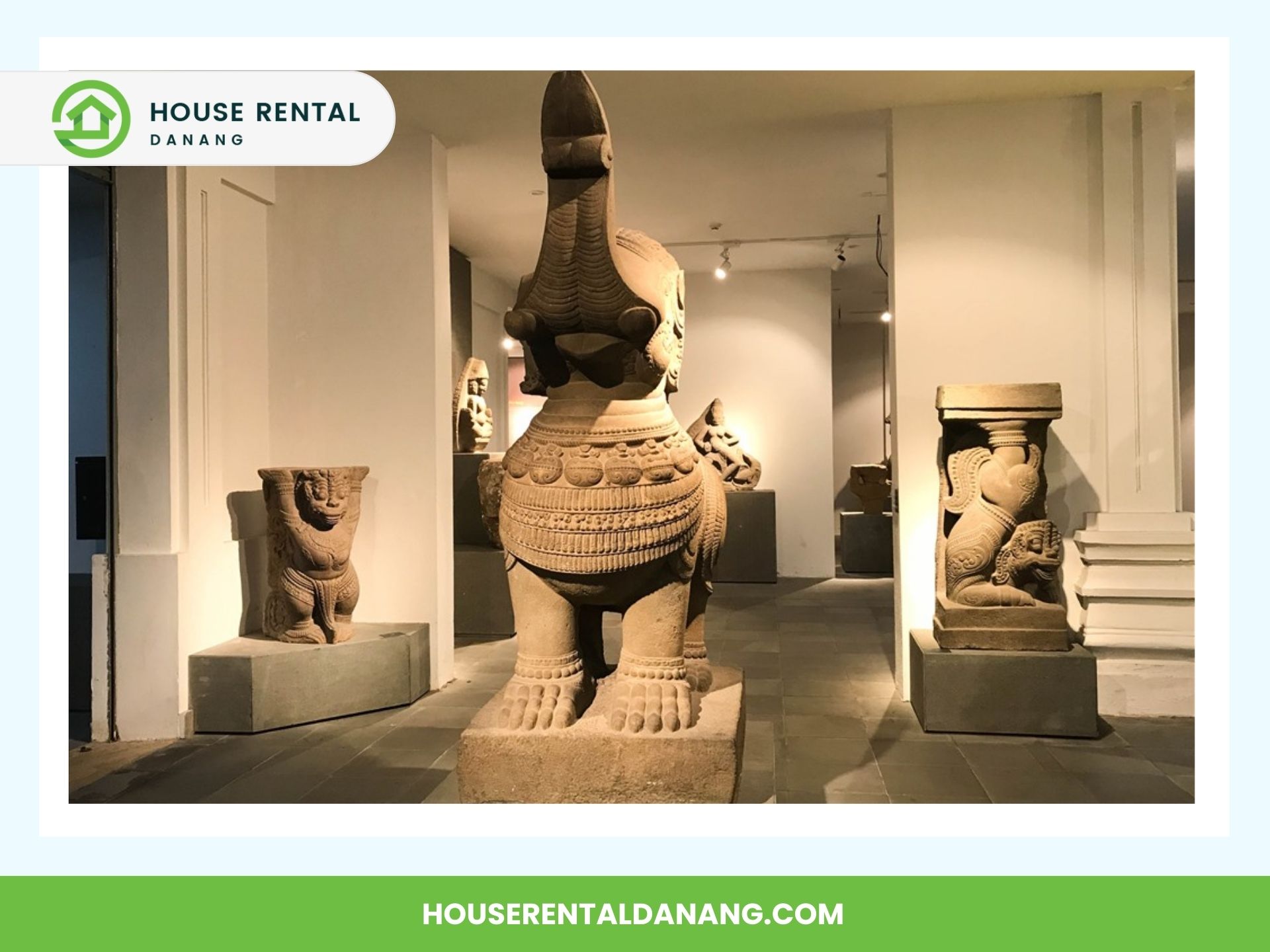 An indoor display at the Danang Fine Arts Museum features intricately carved stone sculptures, including a central figure of an animal with a long neck surrounded by smaller carvings, all illuminated by gallery lighting.