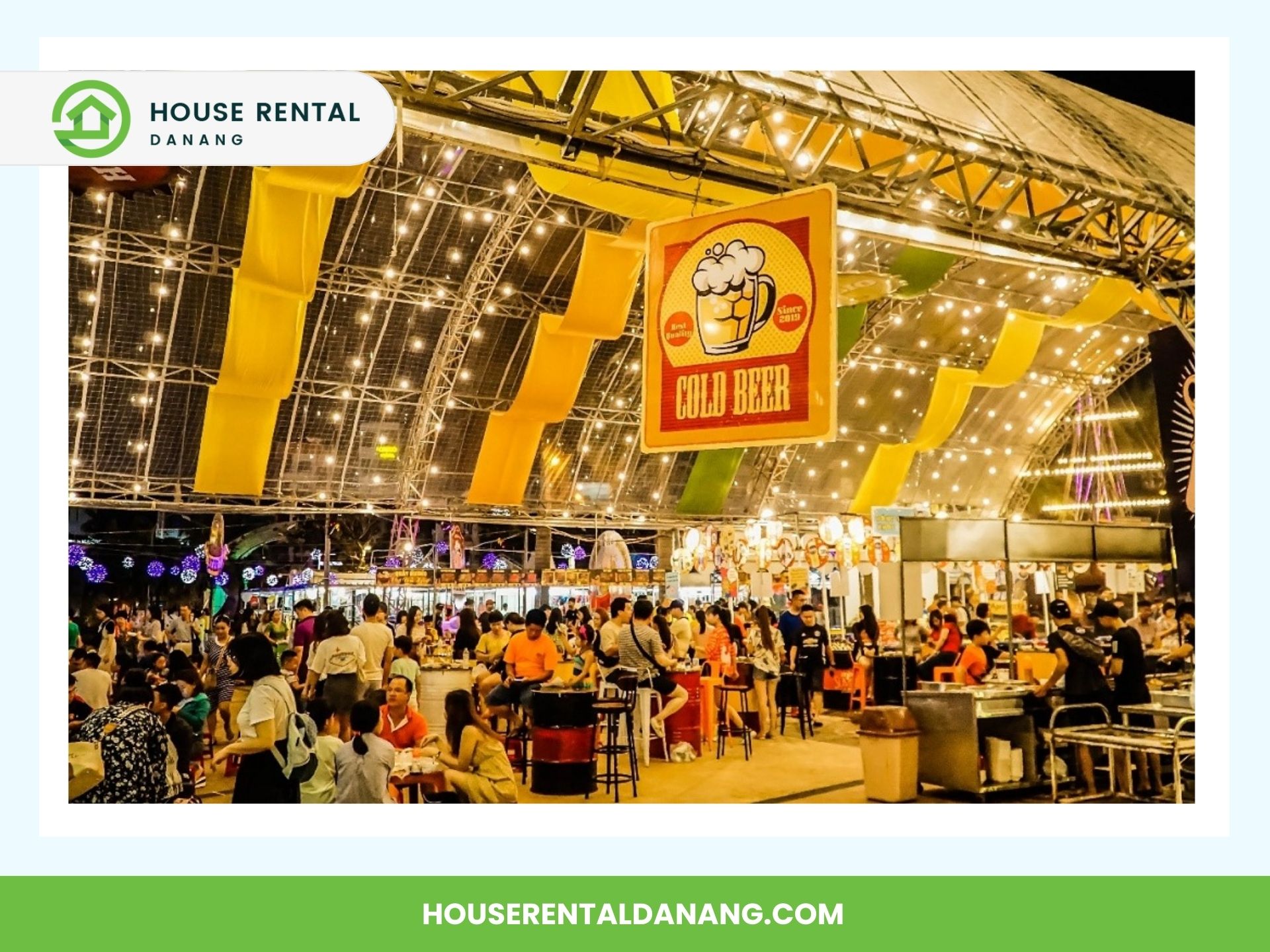 A bustling outdoor beer garden with strings of lights overhead, people seated at various tables, and a prominent "Cold Beer" sign hanging in the center, reminiscent of the vibrant atmosphere you'd find near the Da Nang Fine Arts Museum.