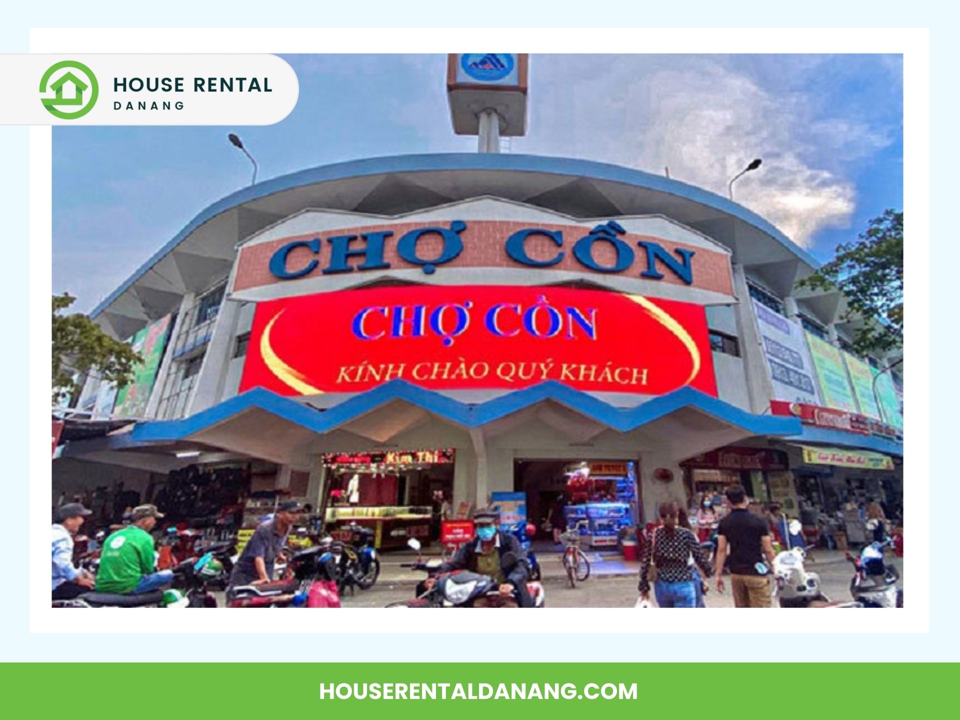 Exterior of Chợ Cồn market with a busy street in front. Motorbikes are parked along the sidewalk and people are walking toward the entrance. A large red sign welcomes visitors to the bustling Con Market.