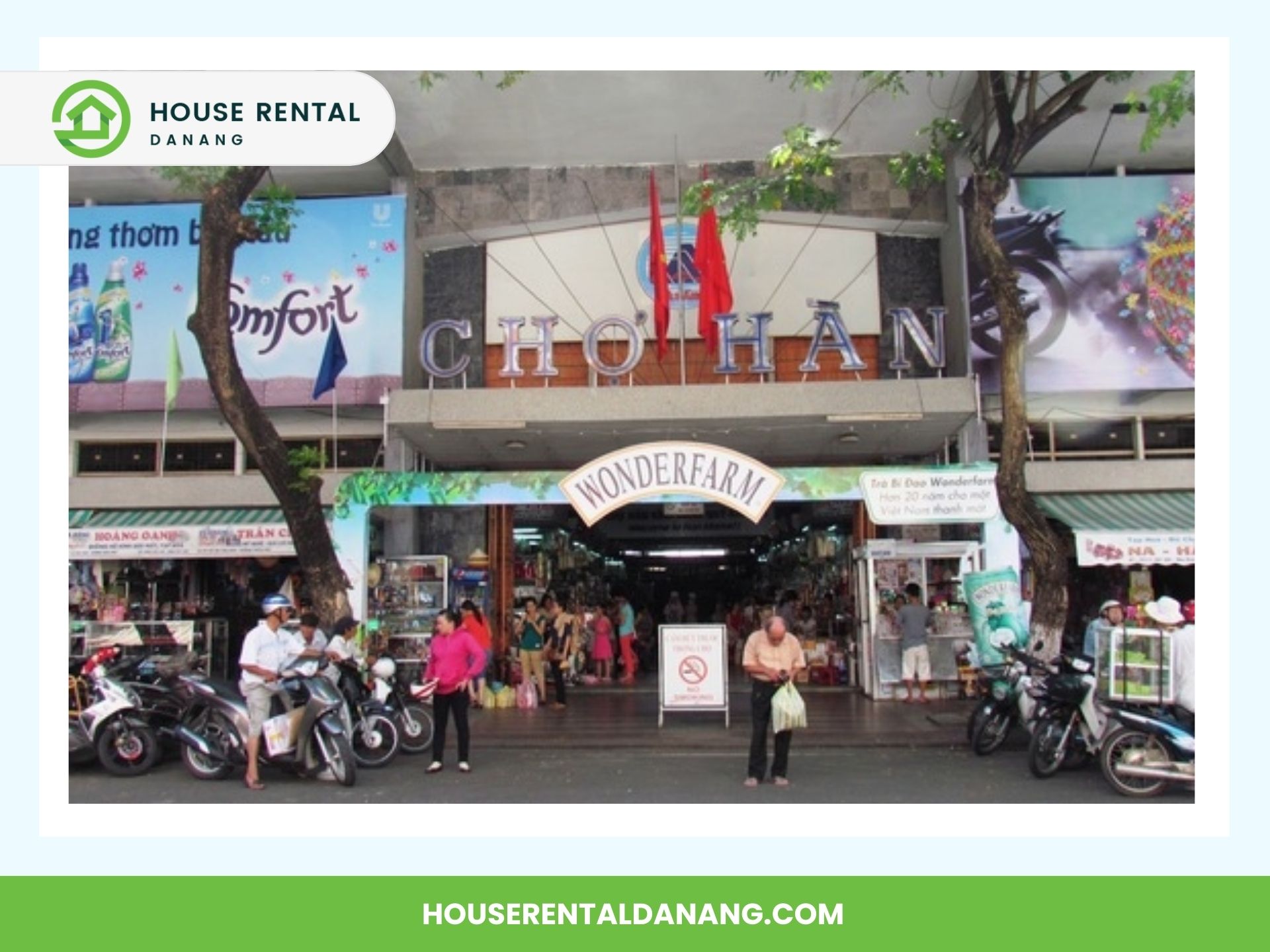 Front view of Han Market Da Nang in the coastal city, with shoppers and motorbikes in front. Two flags and signage are visible above the entrance. HouseRentalDanang.com branding is at the top left and bottom, highlighting its 2024 offerings.