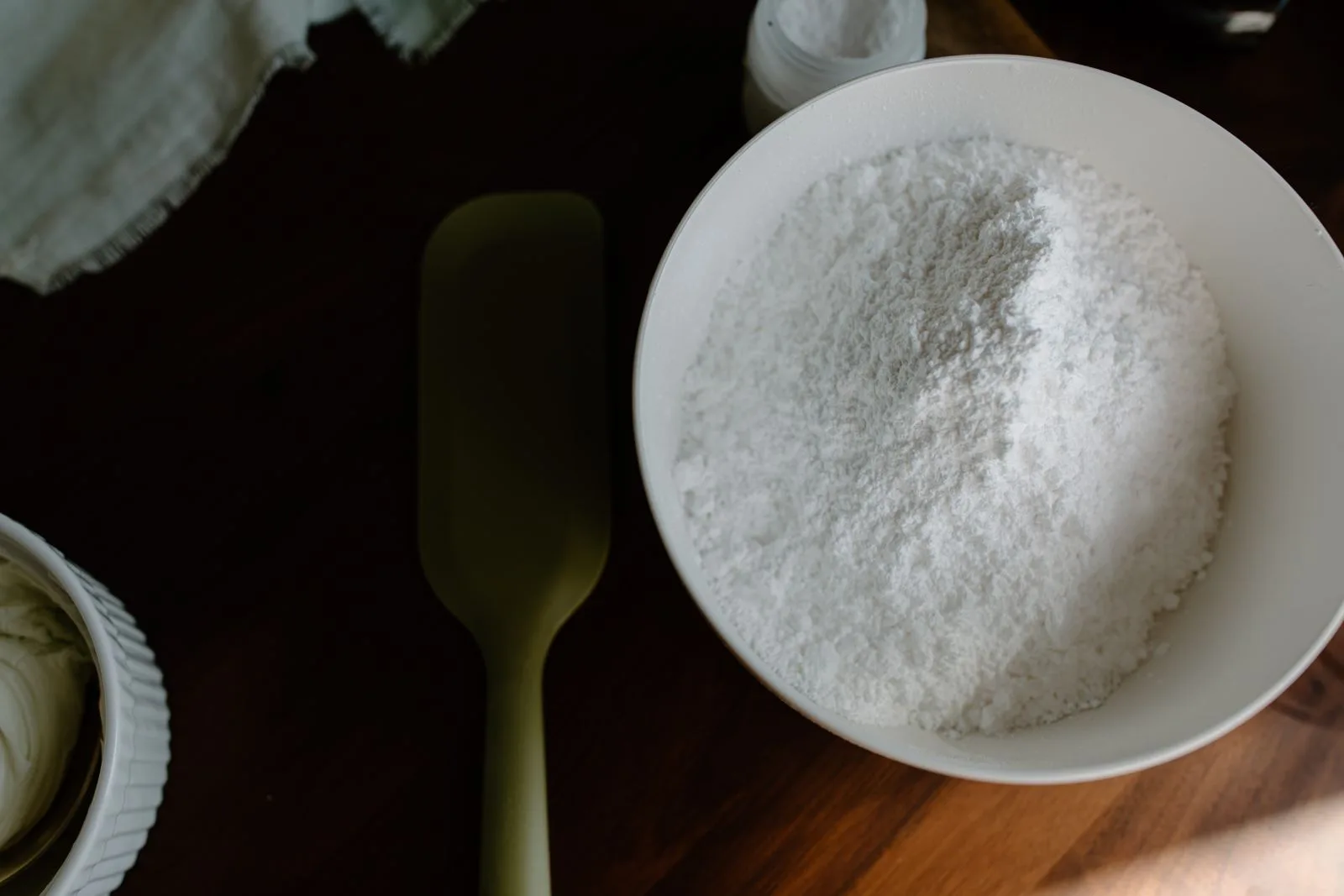 Bột baking soda trắng mịn trong bát sứ trắng, đặt trên bàn gỗ