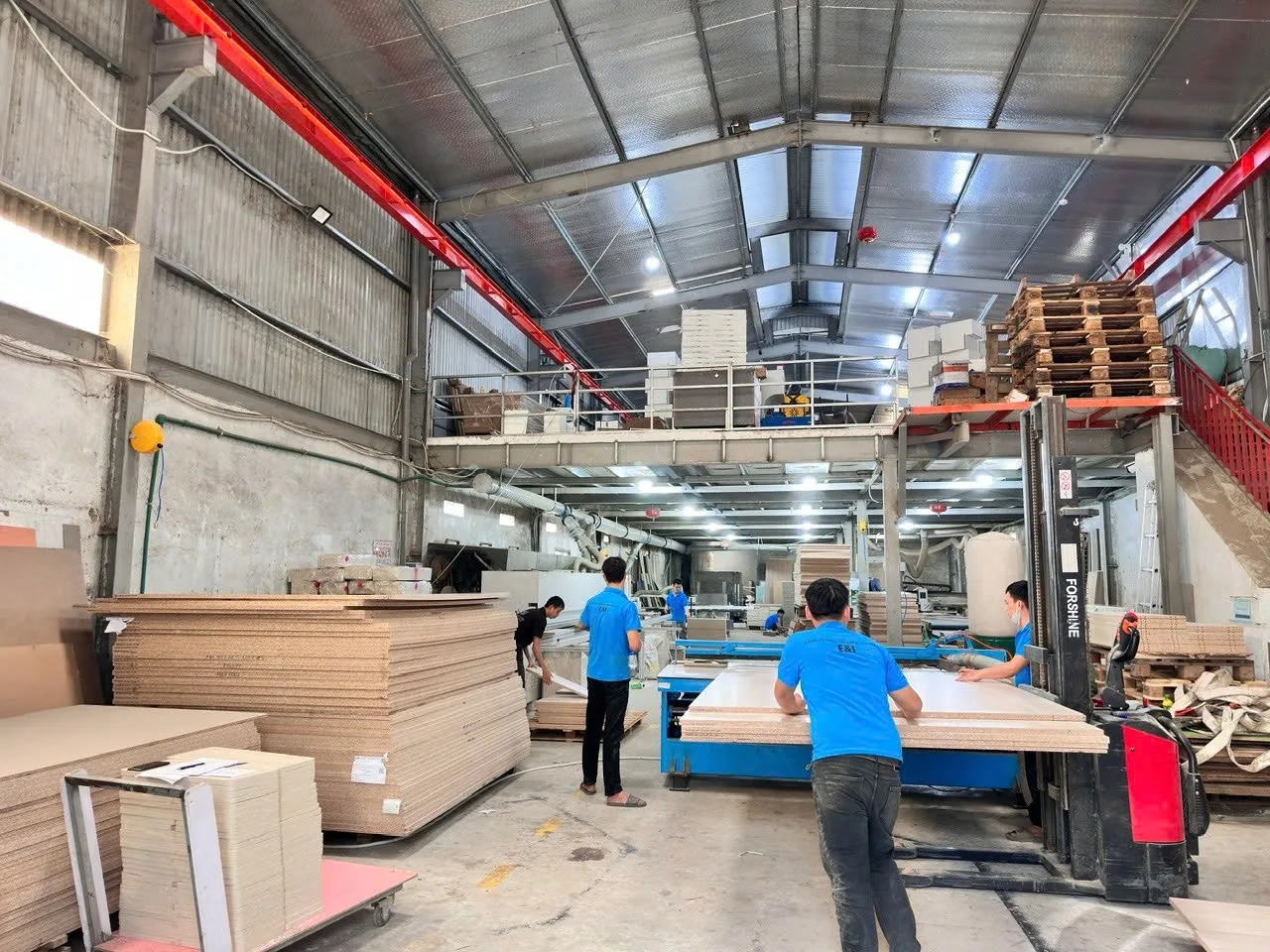 Xưởng sản xuất nội thất của Nội Thất E&I với ván gỗ xếp chồng và thợ đang gia công