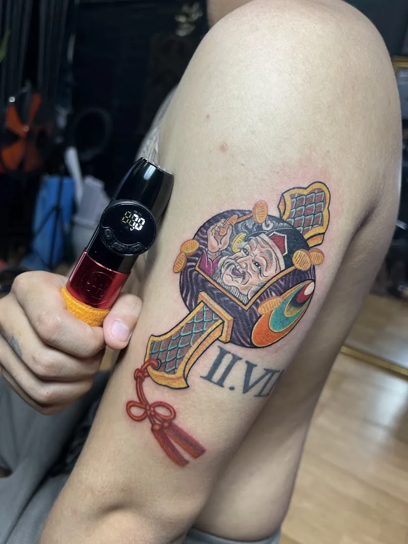 Nghệ nhân cầm máy xăm và lọ mực bên cạnh hình xăm tay màu, tại Bình Tattoo